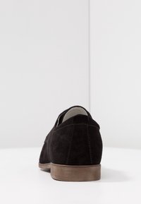 Scarpa in suede nera con punta arrotondata e tacco in legno marrone basso, caratterizzata da dettagli di cucitura discreti e una texture liscia.