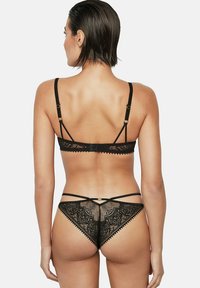 Zwarte kanten lingerieset met een bralette met verstelbare bandjes en een bijpassende string met ingewikkelde bloemmotieven en golvende randen.
