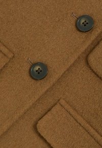 Hnědý vlněný kabát s dvěma tmavými knoflíky, texturovaným povrchem a jednou kapsou na levé straně. Klasický zakázkový design.