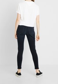 Hubené tmavě modré džíny se zadními kapsami, doplněné o bílé tričko s krátkým rukávem a černé nazouvací boty. Jednoduché a casual stylizace.