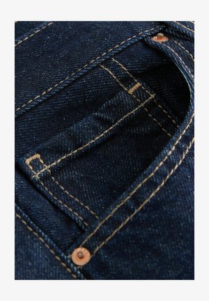 Close-up of dark blue denim jeans pocket with visible stitching and a copper rivet on the top corner.