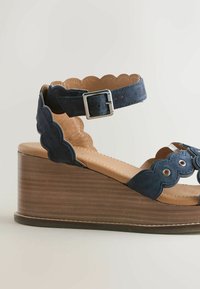 Sandale compensée en daim bleu marine avec brides festonnées, bride de cheville à boucle argentée et talon plateforme effet bois.