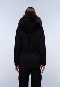 Sort parka-jakke med krave af kunstpels, indsnævret talje, lange ærmer og en glat tekstur. Har justerbar hætte og tætsiddende detalje i stoffet.