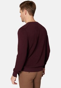 Burgundowa swetrowa struktura z okrągłym dekoltem, prążkowanymi mankietami i dolnym wykończeniem, widok z tyłu. Materiał wydaje się być tkany i oddychający.