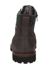 Stivale alla caviglia in pelle marrone scuro con colletto in maglia imbottito, zip laterale e suola in gomma nera robusta, mostrato da dietro.