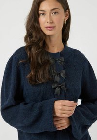 Maglione blu navy con trama, maniche a campana, decorato con quattro fiocchi di nastro nero sulla parte anteriore. Realizzato in morbido materiale a maglia e con vestibilità comoda.