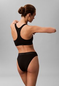 Zwarte sportbeha en hooghengende slipset van zacht materiaal, met een racerback ontwerp en logo banddetails.