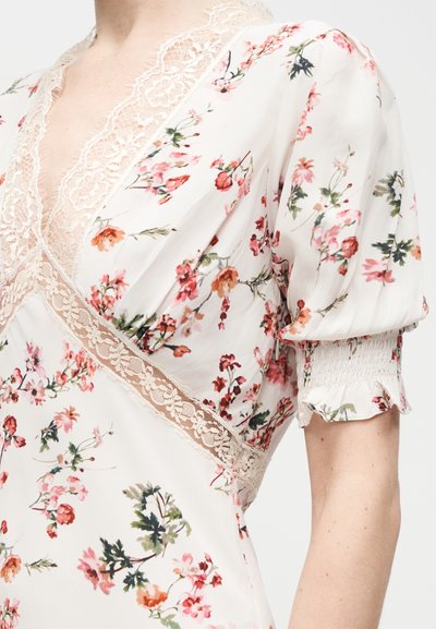 Λευκό φόρεμα με λουλουδάτο σχέδιο σε ροζ και πορτοκαλί αποχρώσεις, δαντέλα κατά μήκος του V-λαιμόκοψη και της μέσης, με φουσκωτά κοντά μανίκια και σφηκοφωλιά στα τελειώματα.