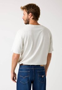 Lysegrå kortærmet t-shirt med rund halsudskæring, parret med mørkeblå jeans med kontrastsyninger og baglommer.