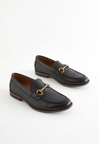 Mocassins en cuir noir avec un bout arrondi, des ornements dorés et une finition texturée. Talon bas et doublure intérieure lisse.