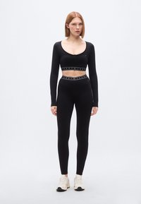 Μαύρο cropped μακρυμάνικο top με στρογγυλή λαιμόκοψη, σε συνδυασμό με μαύρα ψηλόμεσα κολάν με branded ζώνη στη μέση.