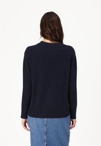 Mørkeblå strikkegenser med rund hals, ribbede mansjetter og kant. Brukt sammen med et lys blått denimskjørt, som viser en myk tekstur.