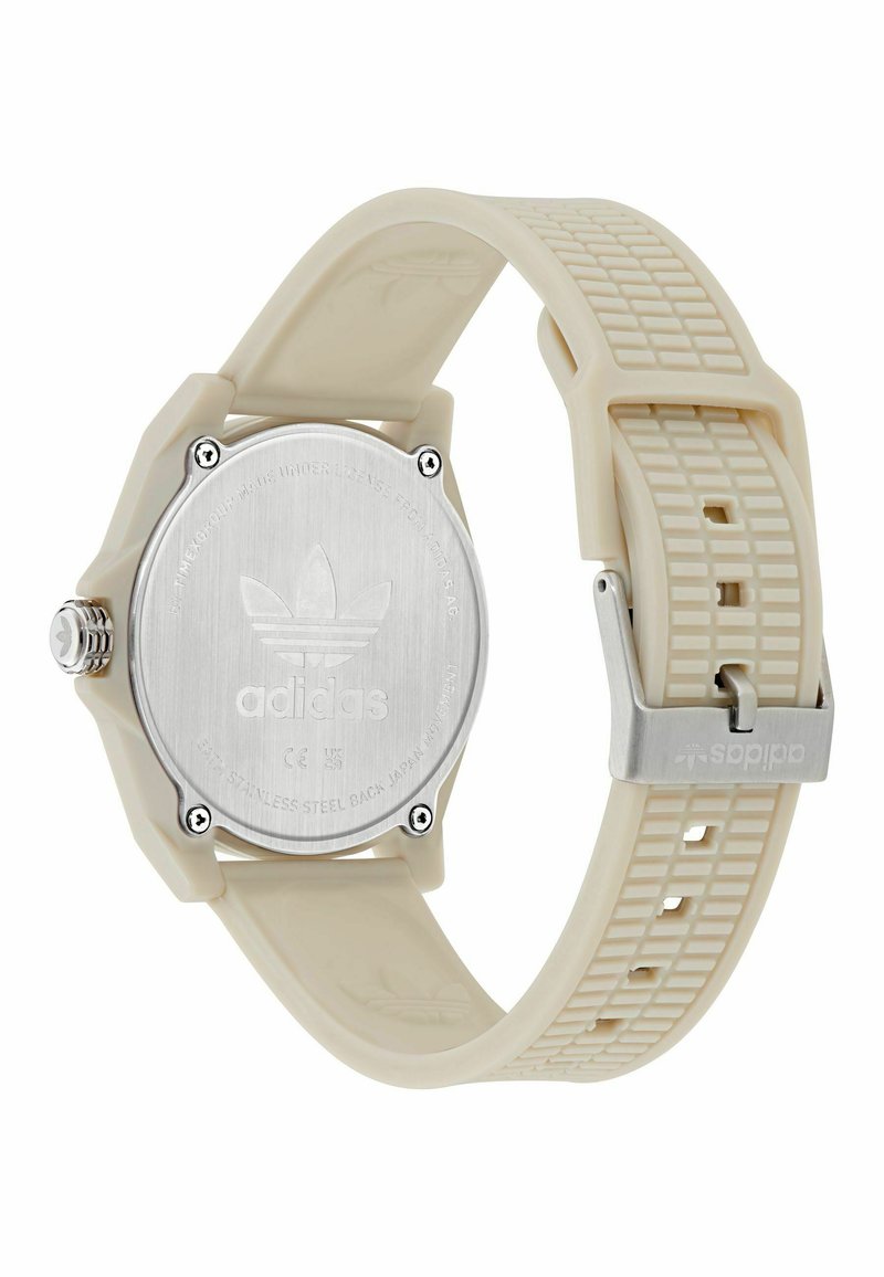 Montre à quartz avec un bracelet en silicone crème, un dos en acier inoxydable et un design texturé. Présente un logo embossé, une boucle métallique et des fixations visibles.
