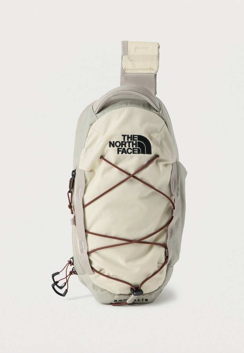 Μπεζ και ανοιχτό γκρι σακίδιο ώμου North Face με ελαστικό κορδόνι που διασταυρώνεται μπροστά και ρυθμιζόμενο ιμάντα σε λευκό φόντο.