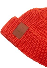 Pomarańczowa wełniana czapka z prążkowanym wzorem oraz brązową skórzaną naszywką z logo góry. Materiał jest miękki i lekko elastyczny.