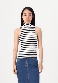 Svart og hvit stripete ermeløs trøye med høy hals og en tettsittende design, kombinert med et blått denimskjørt med en søm i front.