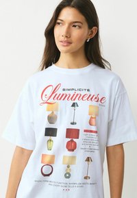 Tricou alb cu un design grafic ce prezintă diferite stiluri de lămpi, inclusiv forme și culori variate, însoțit de un text care evidențiază caracteristicile acestora.