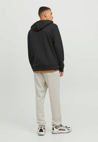 Schwarzer Kapuzenpulli mit Kängurutasche und verstellbarem Kapuzenzug, kombiniert mit hellgrauen Jogginghosen und mehrfarbigen Sportschuhen.