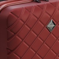 Red polycarbonate suitcase with a quilted texture, featuring a metallic logo plate, black zipper, and angular shape.