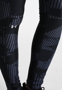 Musta legginsit, jotka on valmistettu joustavasta materiaalista, sisältävät teksturoidun muotoilun ja harmaita raitoja sekä Under Armour -logon. Ei taskuja tai metalliosia.