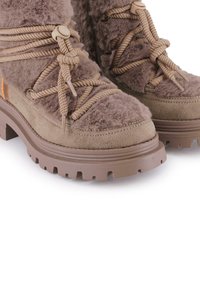 Botas de tobillo marrones con textura suave, paneles de ante y suelas de goma gruesas. Cuentan con cierres de cordones ajustables y un collar acolchado.