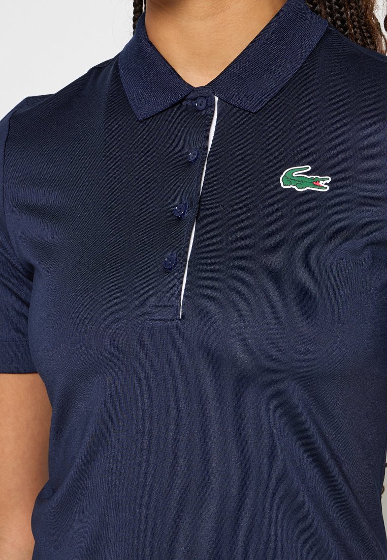 Granatowa koszulka polo z teksturowanej tkaniny, z zapięciem na guziki oraz małym zielono-białym logo krokodyla po lewej stronie na piersi.