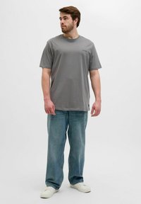 Camiseta gris de manga corta, hecha de una tela suave, con un pequeño logo. Combinada con unos vaqueros holgados de color azul claro y zapatillas blancas.