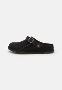 Clog din suede neagră, dotat cu o curea lată cu cataramă, superior texturat și talpă din gumă cu pete pentru aderență. Design clasic și elegant.