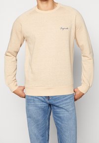 Sudadera beige con un diseño de punto texturizado, cuello redondo y puños acanalados. Presenta un logo azul bordado de "Originals" en el pecho.