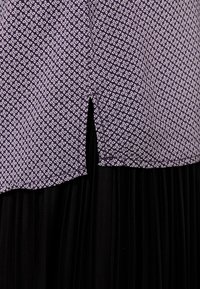 Lila tygtop med vitt geometriskt mönster, med en sidoflik och en svart plisserad underdel. Sömlös övergång mellan materialen.