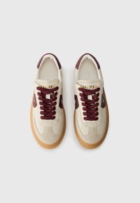 White sneakers with brown accents. Suede and leather materials, flat laces, cushioned collar, and rubber gum sole. Stamped branding visible.