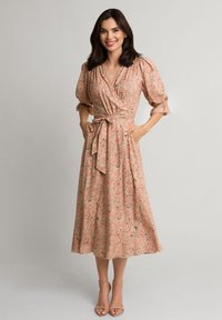 Sukienka kopertowa w jasnoróżowym materiale z kwiatowym wzorem paisley, z bufiastymi rękawami, z paskiem w talii i długości do kostek, w połączeniu z beżowymi sandałami.