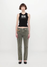 Juodas įpjautas tankas su "Moschino Jeans" logotipu, alyvuogių žalios tiesaus kirpimo džinsai su smėlio spalvos kišene, dėvimi su juodais butais.