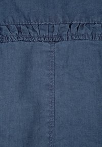 Tissu en denim de couleur bleu profond, avec un surfilage froncé sur le bord supérieur et une texture lisse dans l'ensemble. Couture verticale visible.