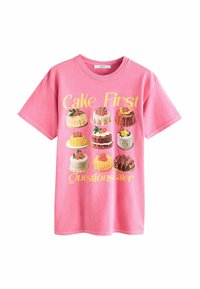 Pink cotton t-shirt featuring an illustration of various cakes, with the text “Cake First Questions Later” in yellow above.