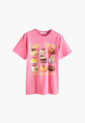 Pink cotton t-shirt featuring an illustration of various cakes, with the text “Cake First Questions Later” in yellow above.