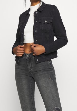Kvinde iført sort cropped denimjakke, hvid cropped sweater og high-waisted falmede sorte jeans med let slid.
