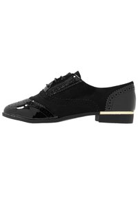 Chaussure oxford noire en daim et cuir verni, présentant des détails perforés, un laçage à l'avant et un talon bas avec un accent doré.