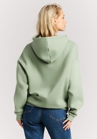 Lichtgroene oversized hoodie met een zachte textuur, voorzien van een grote capuchon en een losse pasvorm, gecombineerd met blauwe denim jeans.