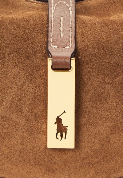 Hnedá semišová látka s koženým remienkom pripevneným k zlatej kovovej etikete s výrezom loga koňa a jazdca.