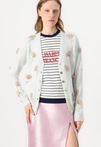 Cárdigan azul claro con bordados florales y lentejuelas, con botones al frente y puños acanalados, usado sobre una camisa a rayas y una falda rosa brillante.