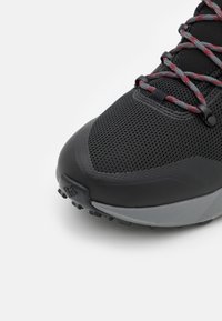 Schwarzer Sportschuh mit einem strukturierten Mesh-Obermaterial, grauem Mittelsohle und roten sowie grauen Schnürsenkeln. Rutschfeste Sohle mit sichtbaren Gummistollen.