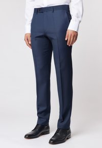 Marineblaue maßgeschneiderte Hosen mit glatter Textur, geradem Schnitt, flacher Front und einem kleinen Knopfakzent am Bund, getragen mit schwarzen Schuhen.