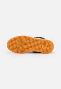 Semelle de chaussure noire avec une semelle extérieure en caoutchouc orange texturé. Présente un motif circulaire et une empreinte de logo près du talon.