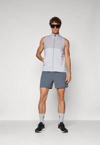 Light gray sleeveless jacket with a zip, paired with dark gray shorts and black sneakers. Textured fabric with two side pockets.