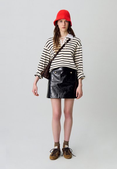 Top de rayas negras y blancas de manga larga, minifalda de cuero negra con bolsillos frontales, gorra tipo cubo roja, calcetines marrones y zapatillas color tan.