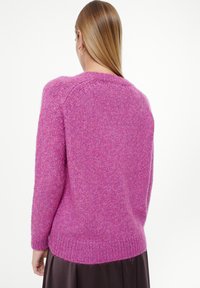 Vrouwelijke fuzzy roze trui met lange mouwen en een ronde halslijn. Beschikt over een geribde zoom en een gestructureerd breipatroon op de schouders en achterkant.