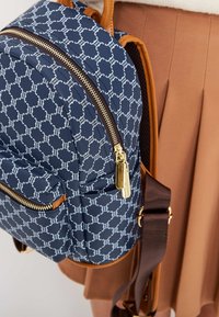 Blå ryggsäck med mönster, guldiga dragkedjor och bruna läderdetaljer. Har två ytterfickor och en vadderad axelrem.