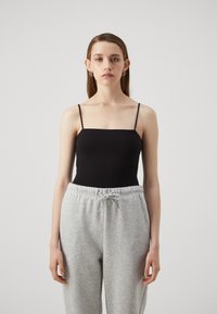 Svart cami med tynne stropper, kombinert med grå joggebukser. Toppen har en tettsittende design, mens buksene har strikk i livet og en myk tekstur.
