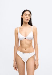 Biele trojuholníkové braletové podprsenky s nastaviteľnými ramienkami a logom na prednej strane; biele nohavičky so zodpovedajúcim logom na páse. Hladká textúra.